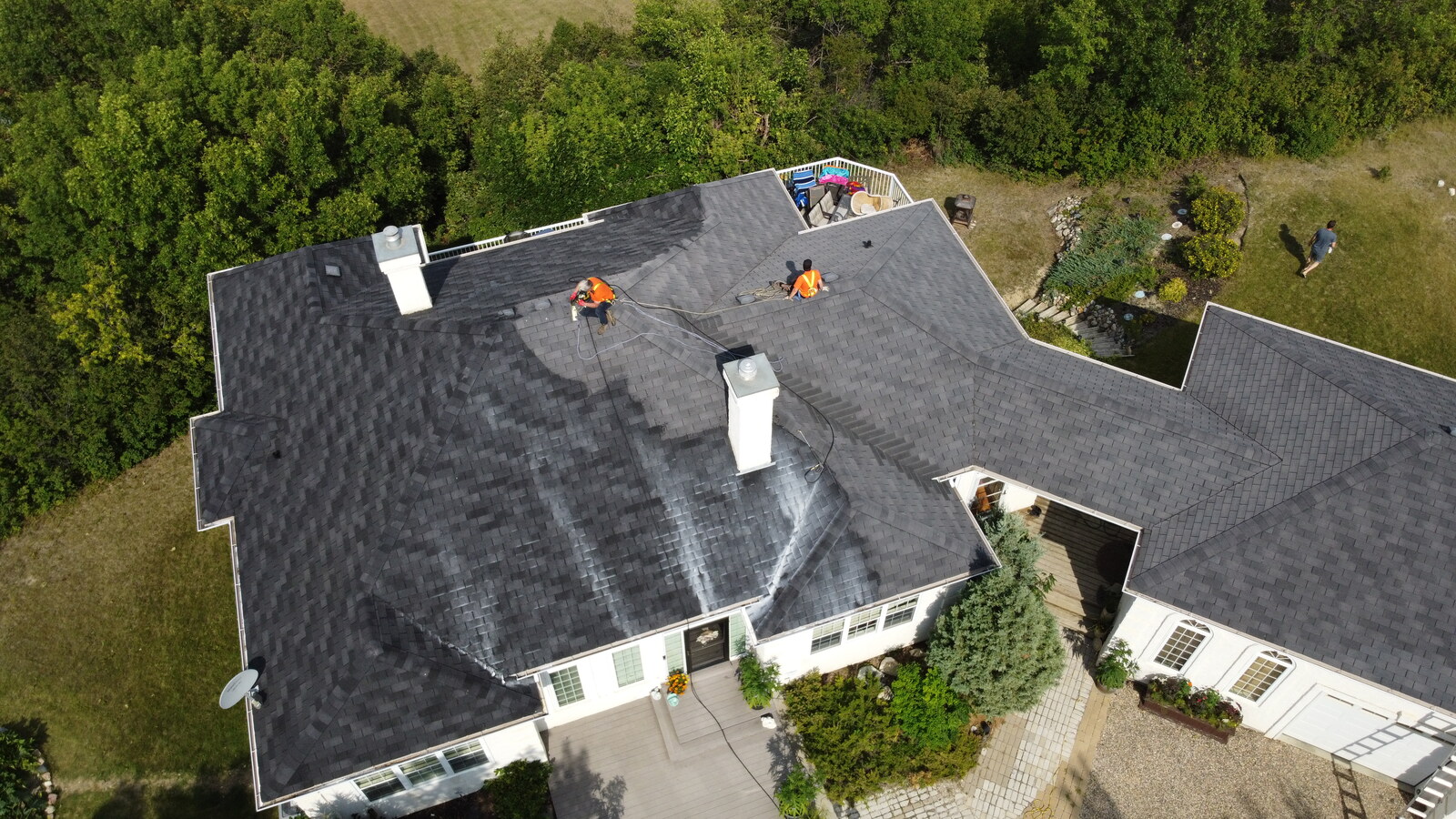 Aerial view of a Roof ReNU crew applying Peak 301 rejuvenation treatment, with the wet application line visible on the shingles.